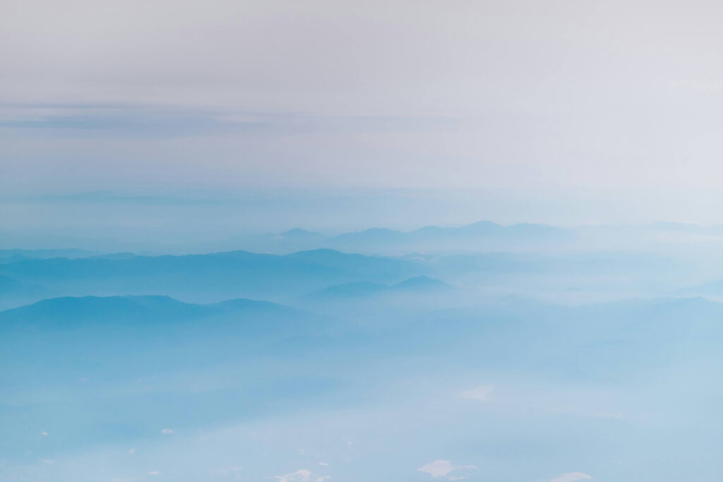 Blå bergskedjor som tonar bort i dimma under en mjuk, molnig himmel.